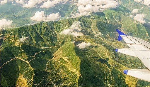 Aerial view of the green vegetation covered great Himalayas from the plane. Visible are the treacherous roads and the floating cumulus clouds.